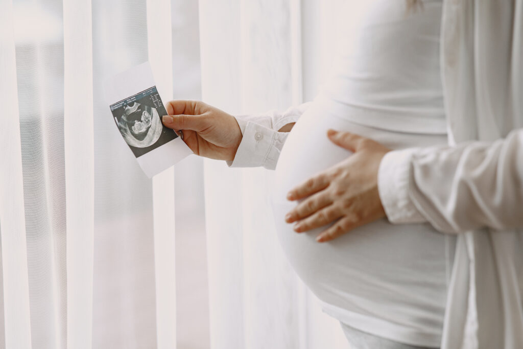 pregnant woman stands by the window and looks at photo