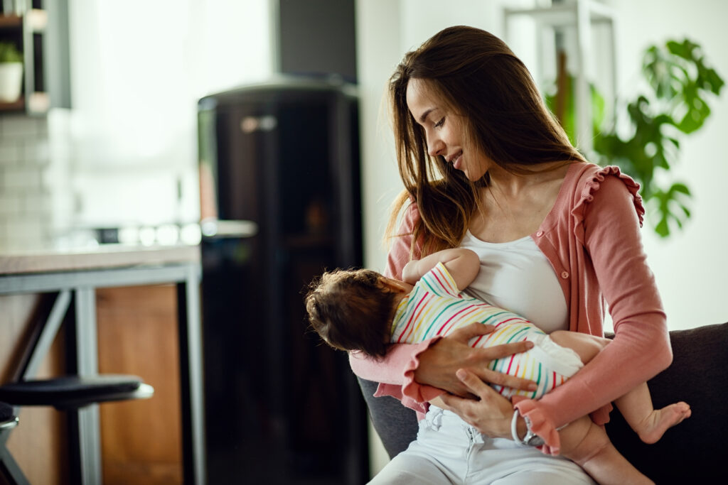 young smiling mother breastfeeding her baby at home.