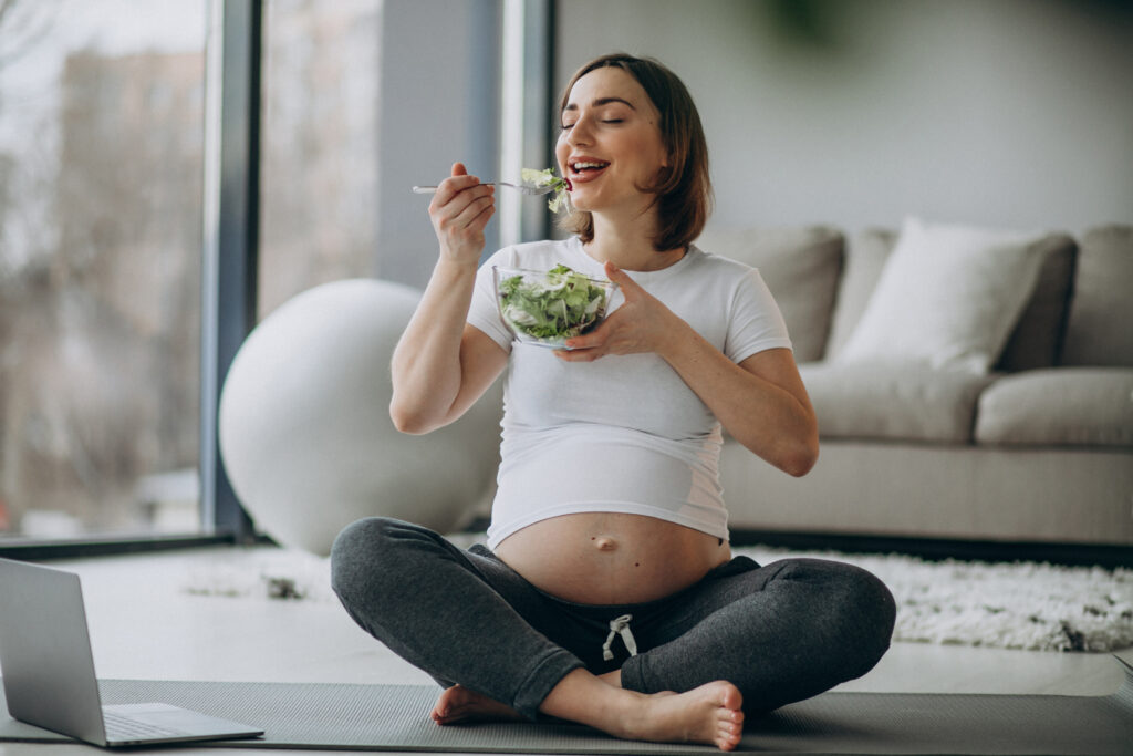 young pregnant woman eating salad at home
